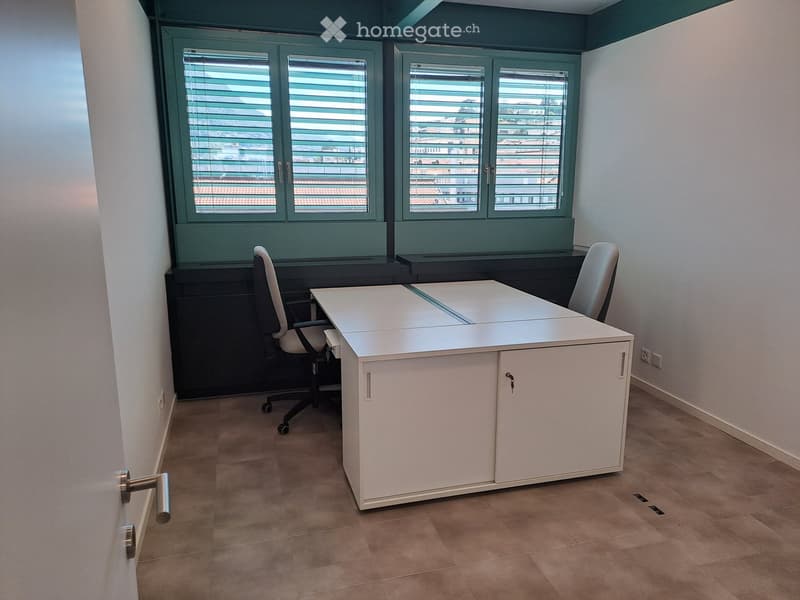 Office space with a white desk, two chairs, large windows with blinds, and tiled flooring.