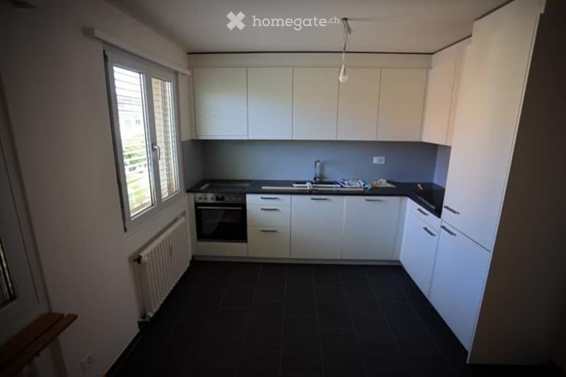 Modern kitchen with white cabinets, black tiled floor, and stainless steel appliances including an oven and sink.