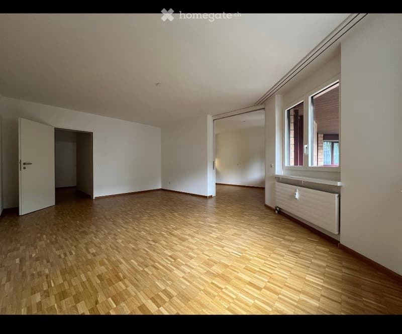 Empty room with wooden flooring, white walls, and large windows. No furniture or equipment present.