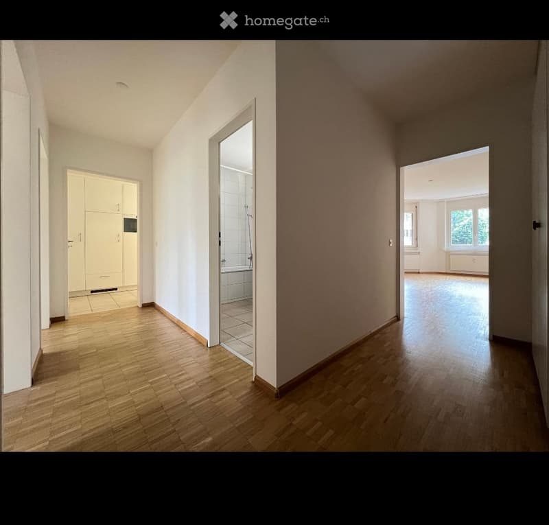 Empty hallway with wooden flooring, white walls, and open doors leading to other rooms. No furniture or equipment visible.
