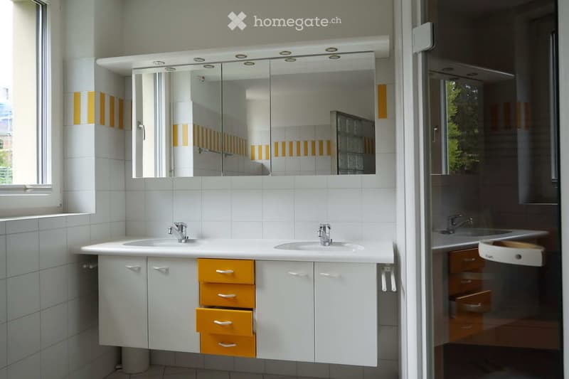 Modern bathroom with white tiles, a double sink vanity with yellow drawers, a large mirrored cabinet with integrated lighting, and a glass-enclosed shower area.