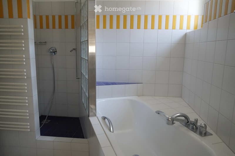 Modern bathroom with a bathtub, shower area, and radiator. The walls are tiled with white and yellow stripes, and the floor is tiled in a contrasting dark color.