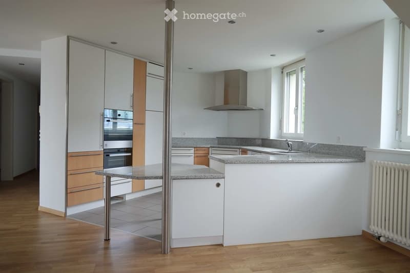 Modern kitchen with white cabinets, granite countertops, stainless steel appliances, and wooden flooring.