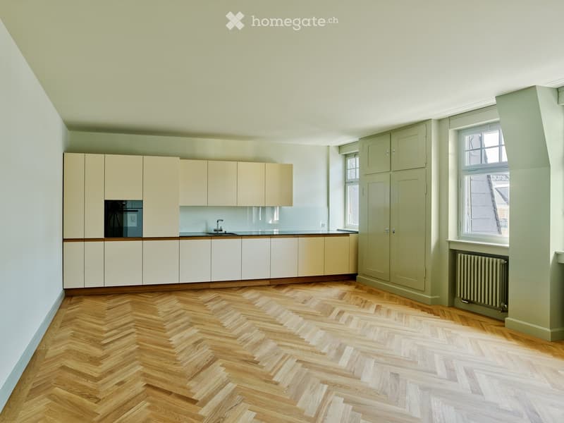 Modern kitchen with light-colored cabinets, herringbone wooden flooring, and a sleek countertop.