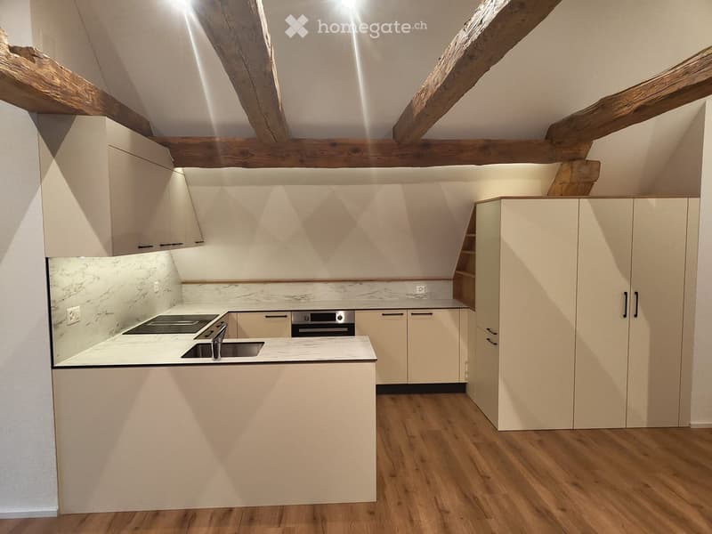 Modern kitchen with light-colored cabinets, marble backsplash, and wooden flooring. Features include a sink, faucet, and built-in oven.