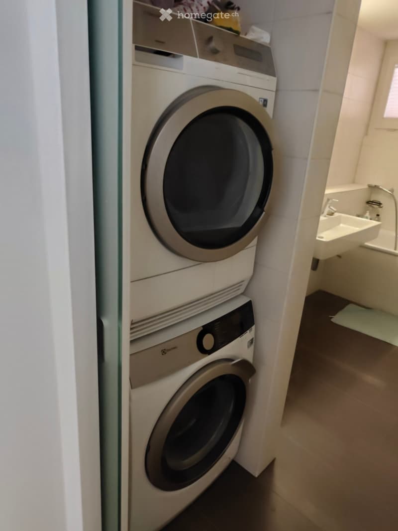 A compact bathroom with a stacked washing machine and dishwasher unit, a white sink, and tiled walls.