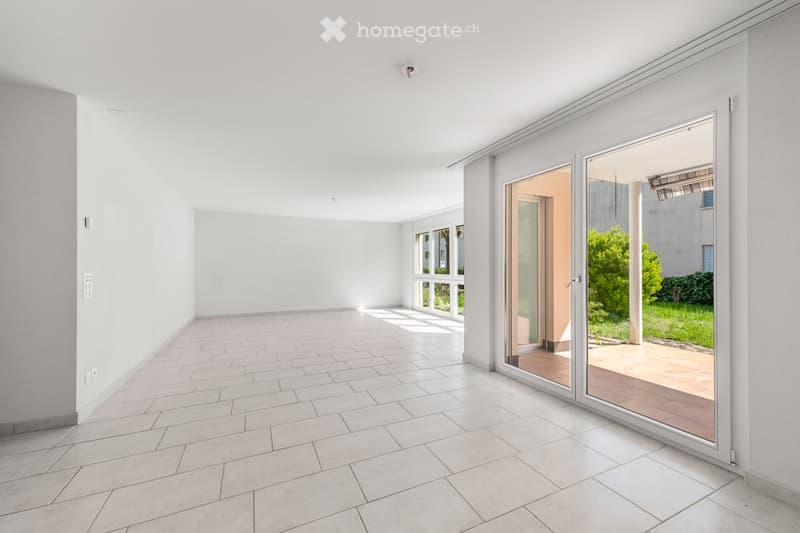 Empty room with white tiled flooring, large sliding glass doors leading to an outdoor area, and white walls.