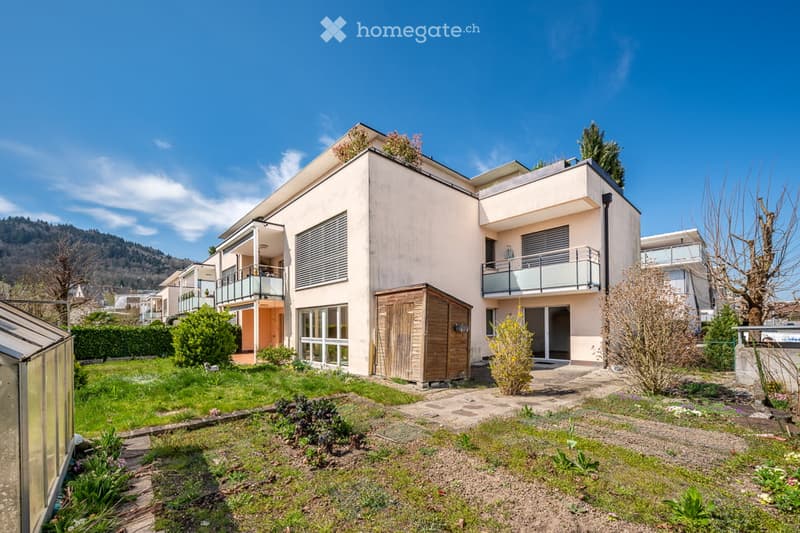 Modern two-story building with balconies, surrounded by a well-maintained garden and trees.