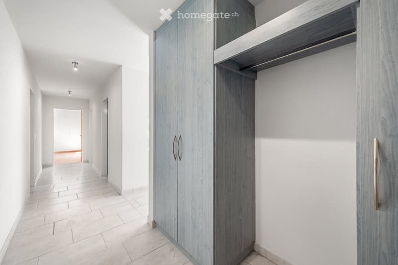 Empty hallway with white walls, tiled floor, and built-in closet with wooden doors and shelves.