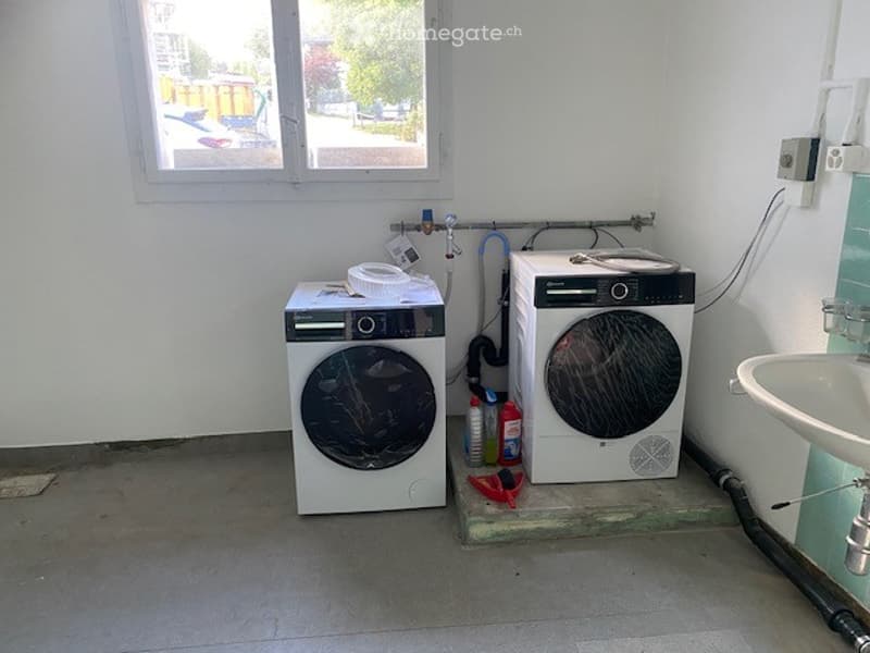 A small utility room with a washing machine, dishwasher, and sink, visible pipes and cleaning supplies.