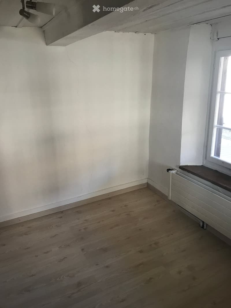 Empty room with wooden flooring, white walls, and a single window with a radiator below it.