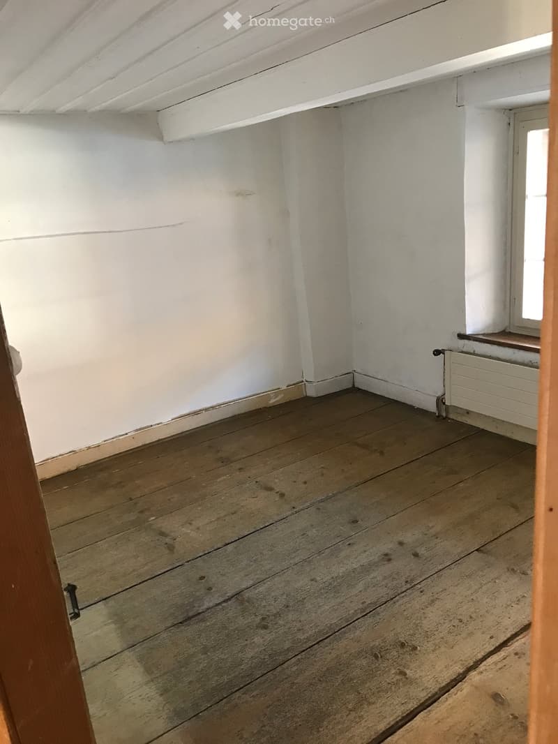 Empty room with wooden floor and white walls, featuring a radiator and a small window with a wooden sill.