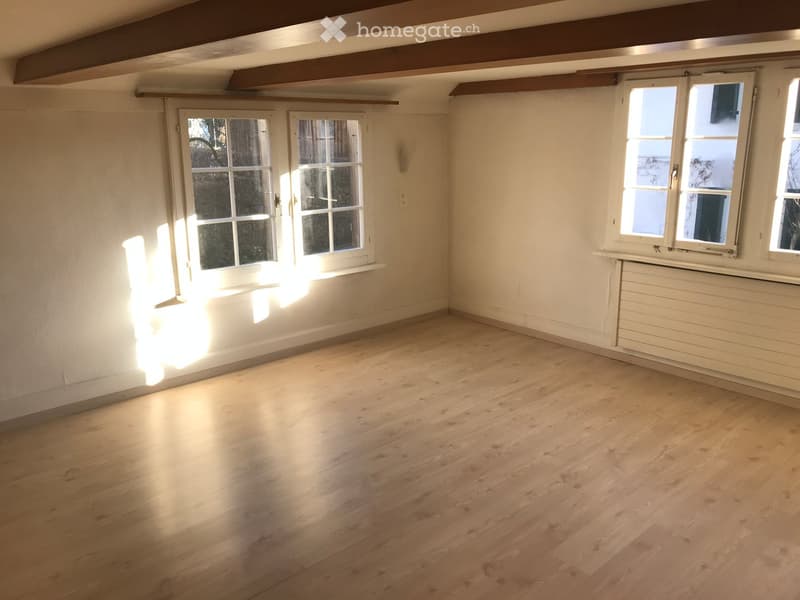 Empty room with light wooden flooring, white walls, and multiple windows allowing natural light to enter.