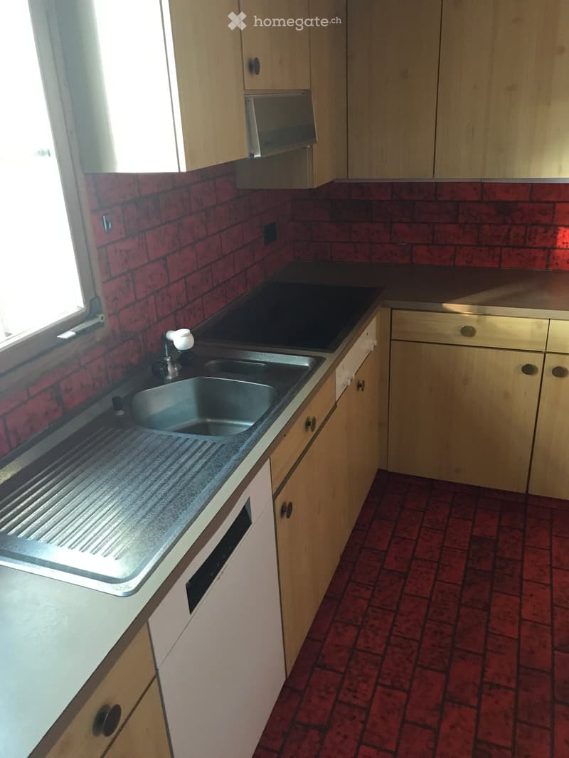 Kitchen with red brick walls, wooden cabinets, stainless steel sink, and a dark countertop.