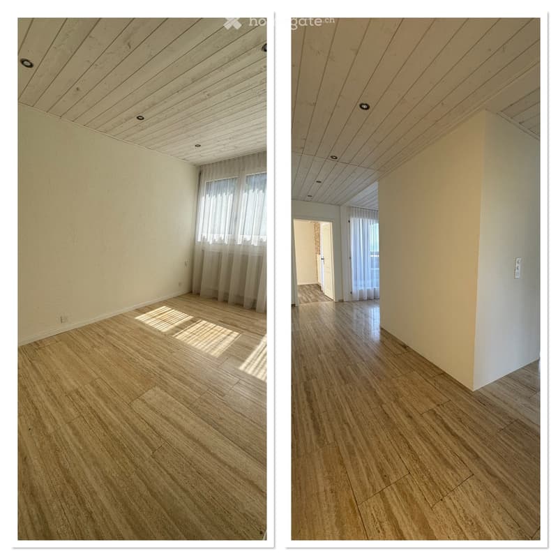 Empty room with wooden flooring, white walls, and a wooden slatted ceiling. Natural light filters through sheer curtains on a window.