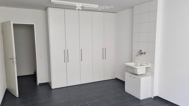 Modern bathroom with white tiled walls, dark tiled floor, white sink on a cabinet, and large white storage cabinet.