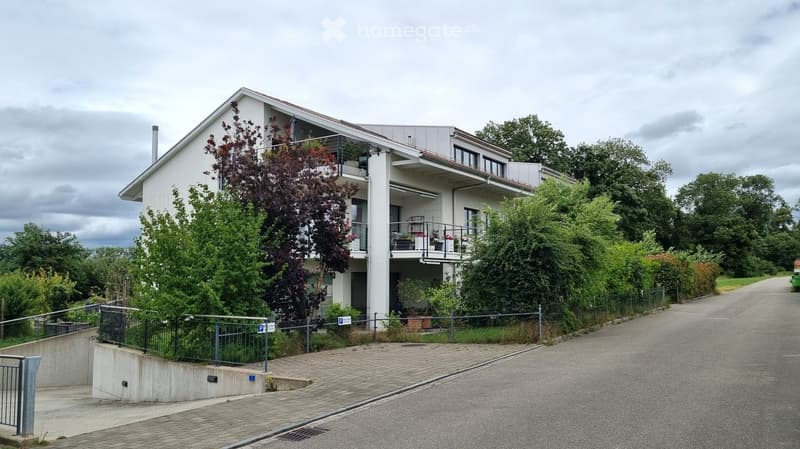Two-story house with white exterior, multiple windows, balconies, and surrounding greenery.