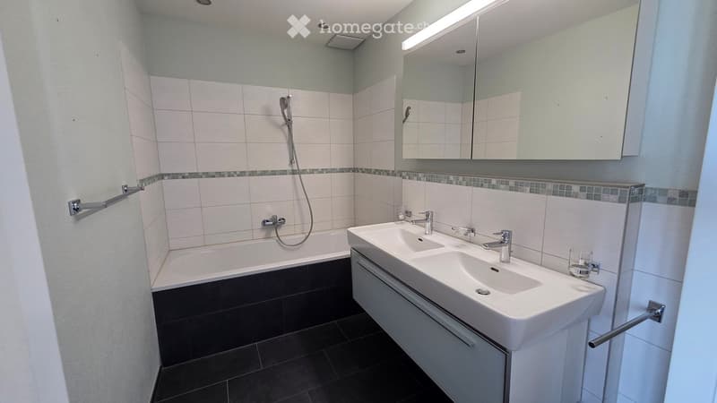 Modern bathroom with a bathtub, double sink, large mirror, and glass on the counter.