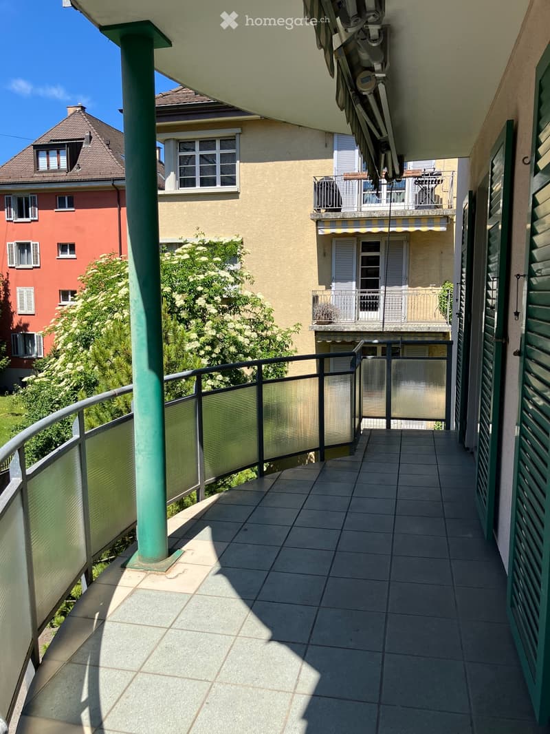 Balcony with tiled floor, metal railing, and view of neighboring buildings and greenery.