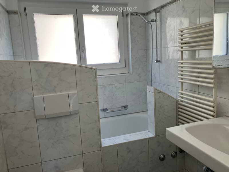 Modern bathroom with marble tiles, a shower area, a sink, and a radiator.