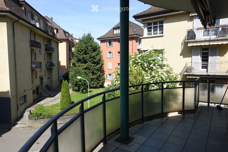 Balcony overlooking a residential area with multi-story buildings, greenery, and a small garden below.