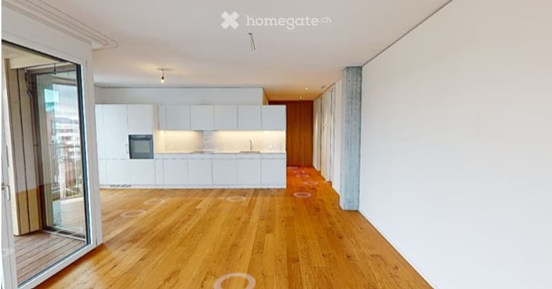 Open-plan kitchen and living area with white cabinetry, wooden flooring, and large glass doors leading to a balcony.