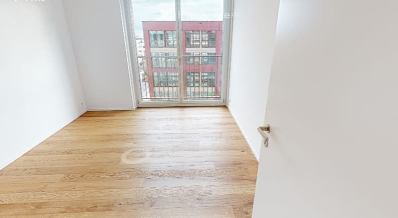 Empty room with wooden flooring, white walls, and large glass sliding doors leading to a balcony.