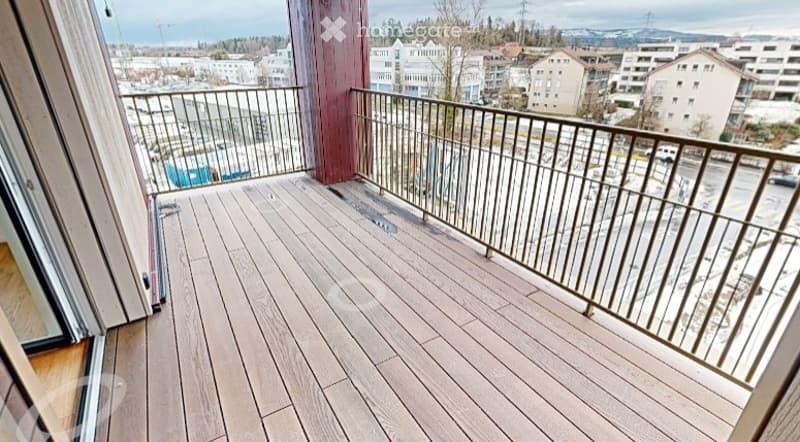 Balcony with wooden decking, metal railing, overlooking a cityscape with buildings and parking area.