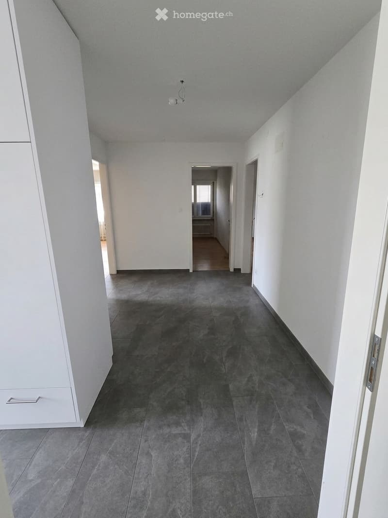 Empty hallway with grey tiled floor, white walls, and several doors leading to other rooms.