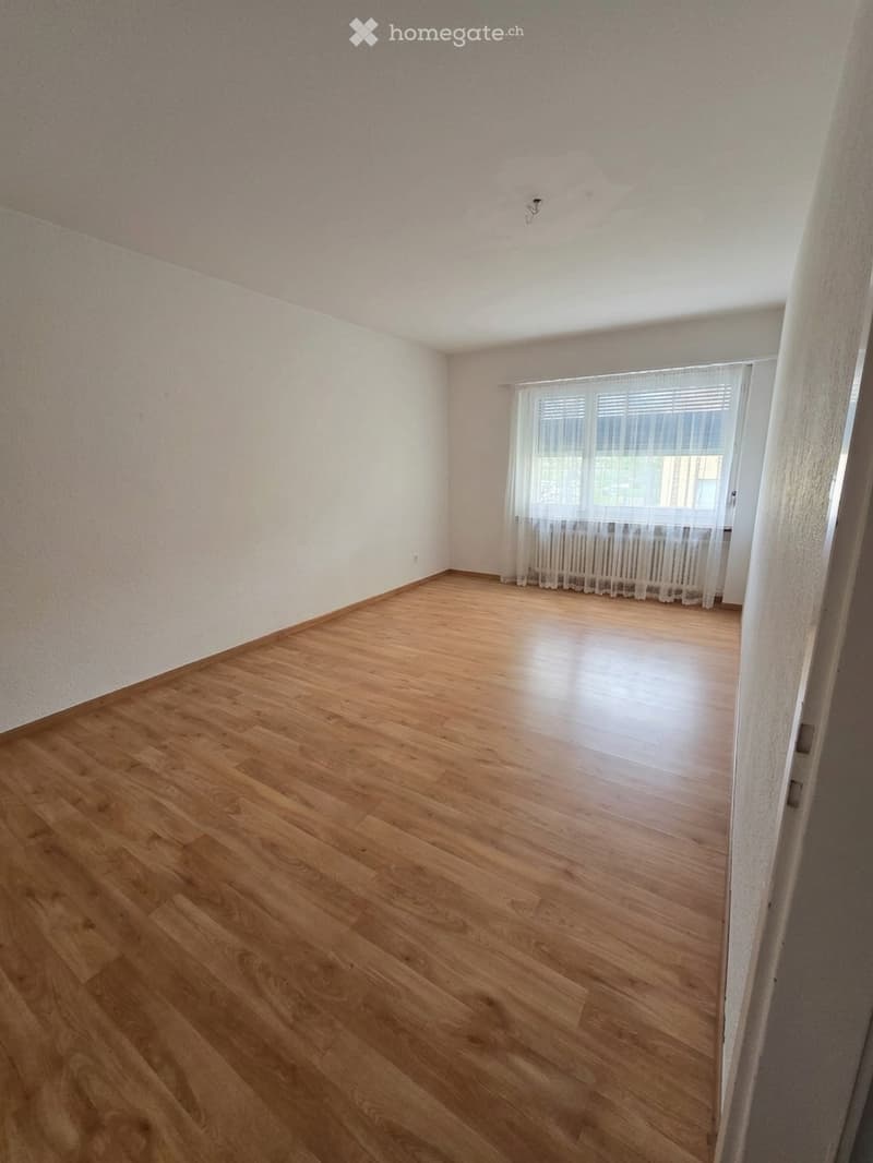 Empty room with wooden flooring, white walls, and a window with sheer curtains. No furniture or equipment is present.