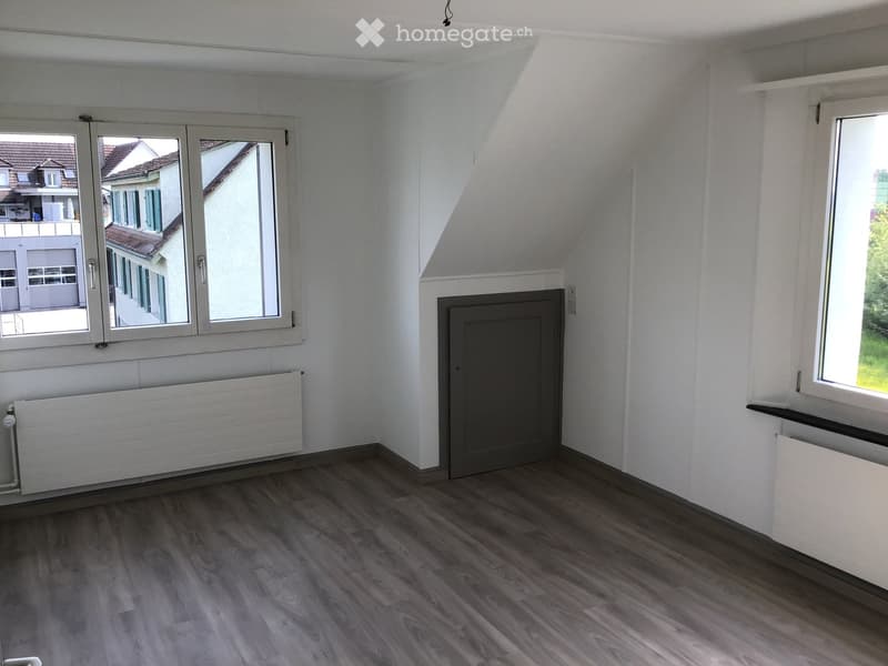 Empty room with wooden flooring, white walls, large windows, and radiators.