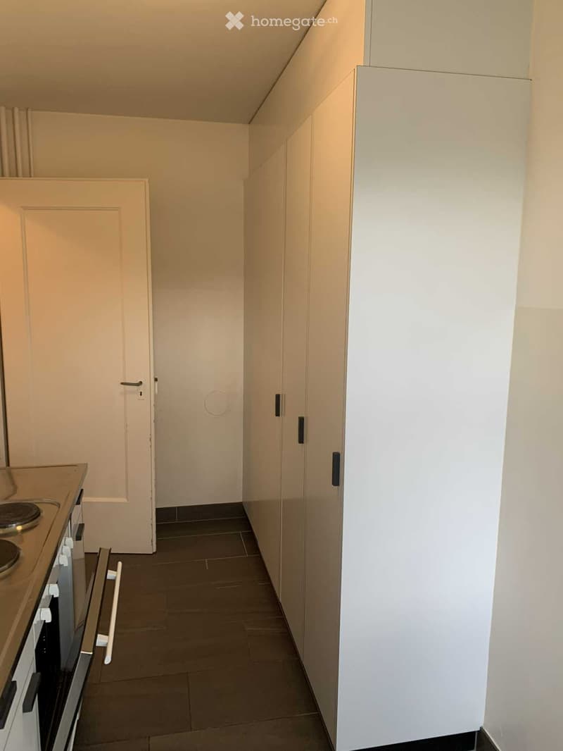 Modern kitchen with white cabinets, dark tiled floor, and a built-in oven on the left side.