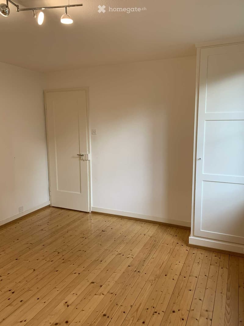 Empty room with wooden flooring, white walls, and two doors.