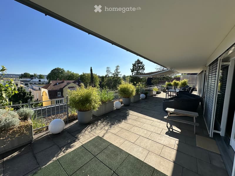 Balcony with tiled floor, metal railing, potted plants, a round table with chairs, a bench, and decorative balls.