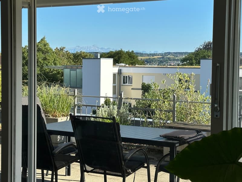 Balcony with a table and chairs, overlooking a scenic view of mountains and greenery.