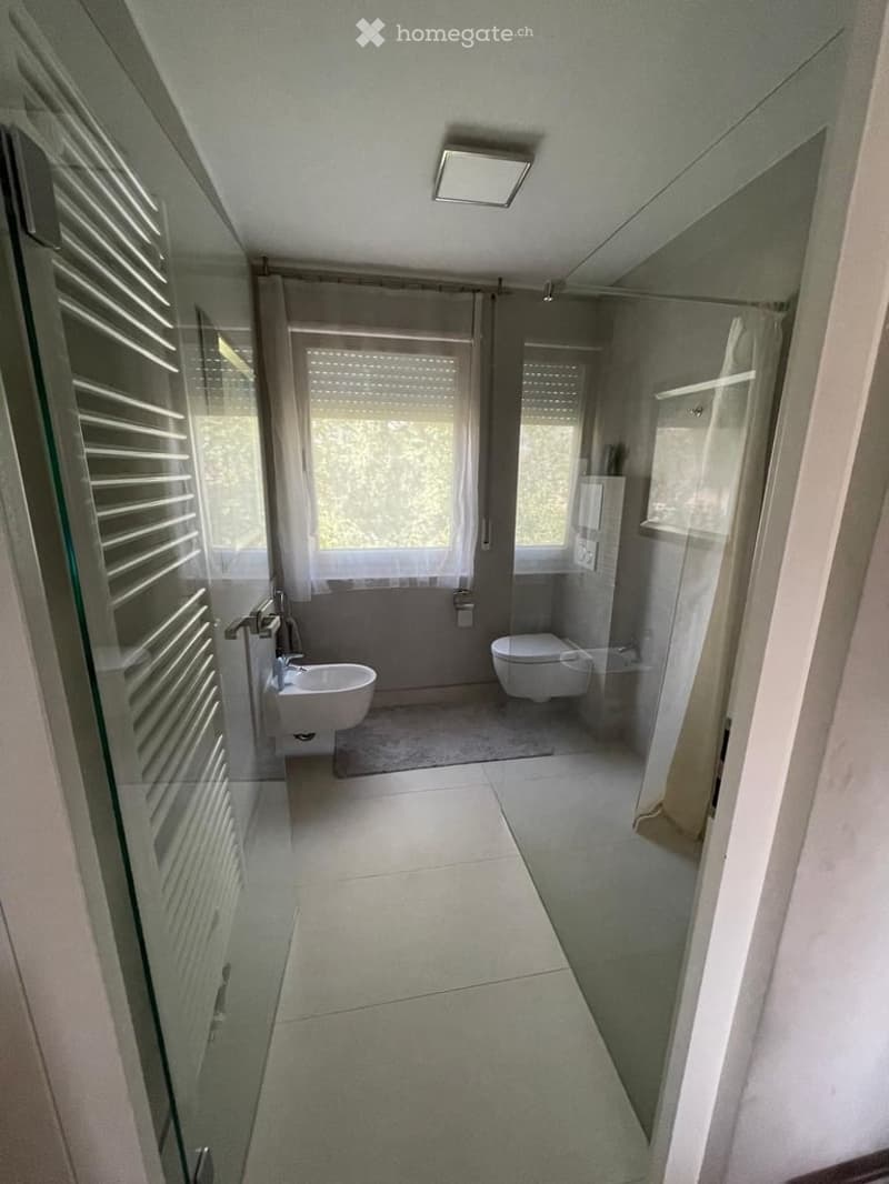 Modern bathroom with a white tiled floor, a sink, a toilet, a shower area with glass doors, and a radiator on the left side.