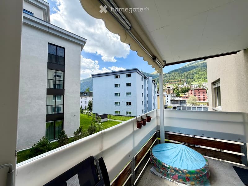 Balcony with a view of a residential area, mountains, and a covered seating area with a small inflatable pool.