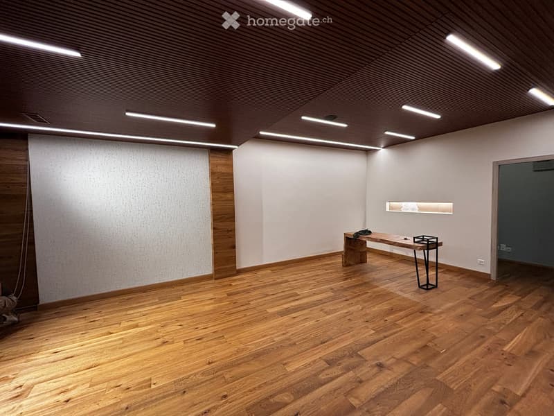 Minimalist room with wooden flooring, white walls, and a single bench with a small table.