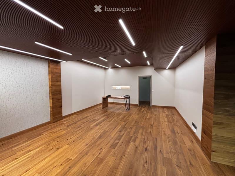 Modern, minimalist room with wooden flooring, white walls, and recessed lighting. Features a small table and a stool.