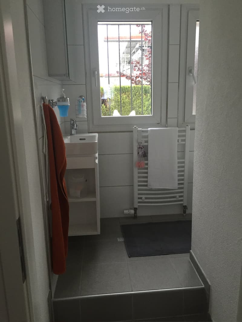 Bathroom with a sink, faucet, towel, radiator, soap dispenser, and towel rack. The room has tiled walls and a window with bars.