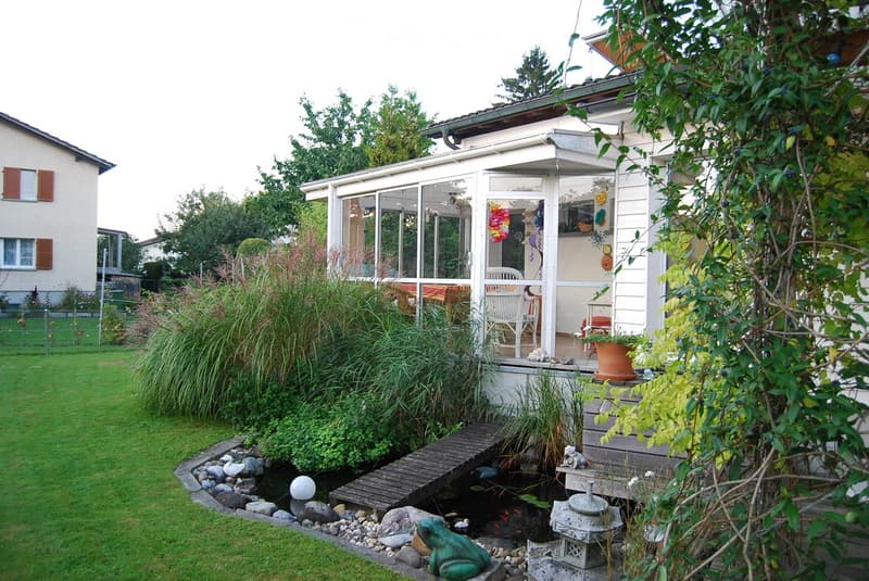 Garden with a pond, stepping stones, decorative frog, and a covered patio area with chairs and a table.