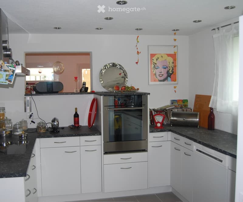 Modern kitchen with white cabinets, granite countertops, stainless steel appliances, and various kitchen items including a bottle, plate, jars, and a framed picture on the wall.