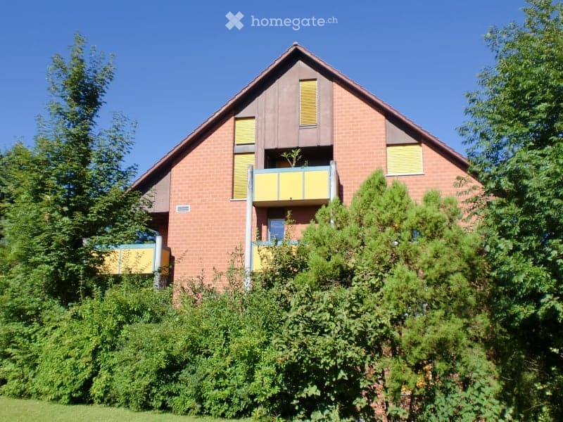 Two-story brick house with a pitched roof, yellow shutters, and a balcony on the upper floor.