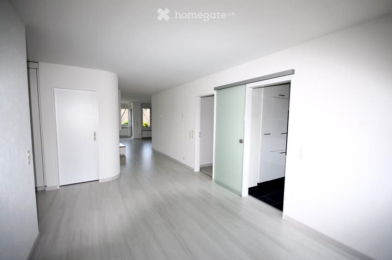 Empty hallway with white walls and floor, closed doors and a sliding glass door.