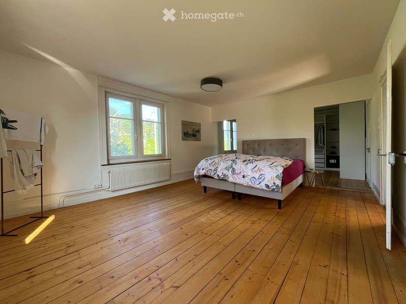 Bedroom. Bright bedroom with wooden flooring, large window, bed with floral duvet, wardrobe, small stool, radiator, and coat rack.