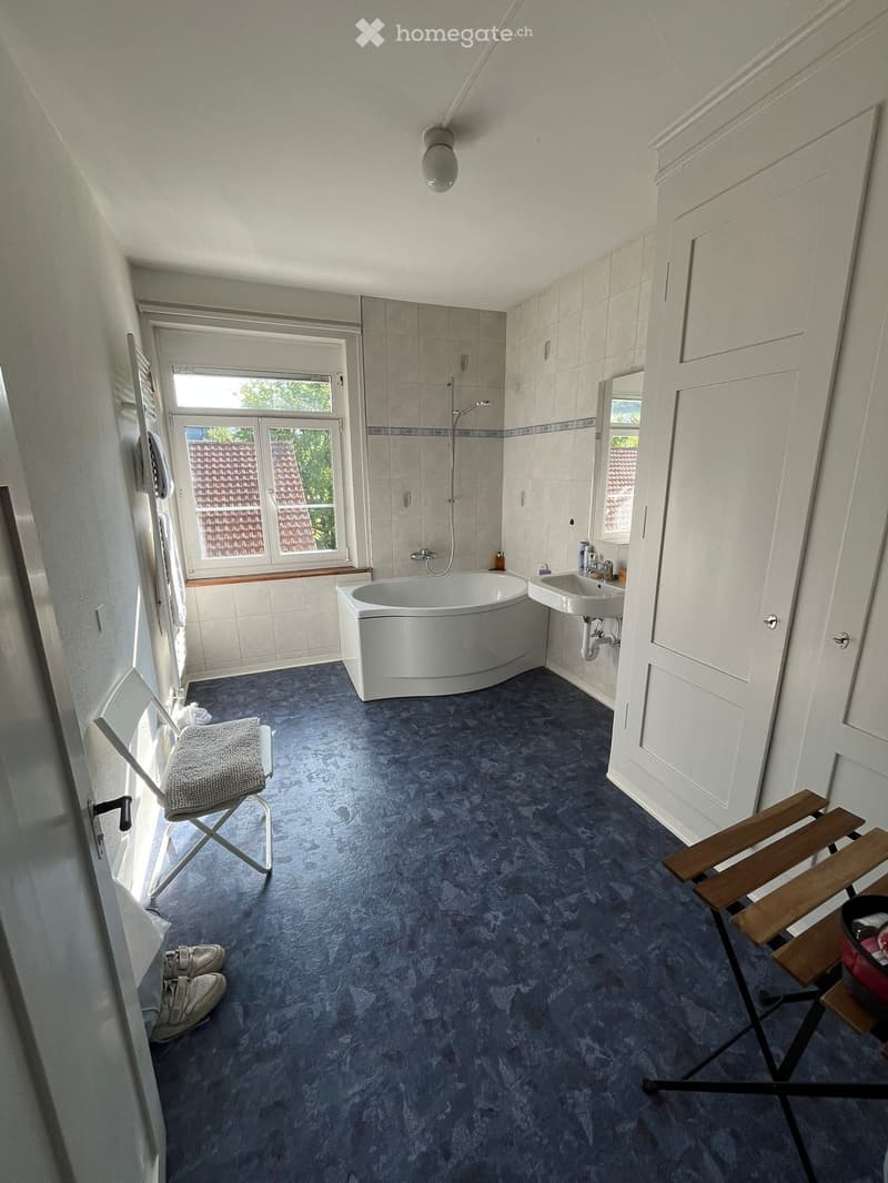 Bathroom. Bathroom with a white bathtub, sink, window, and a small chair and stool near the door.