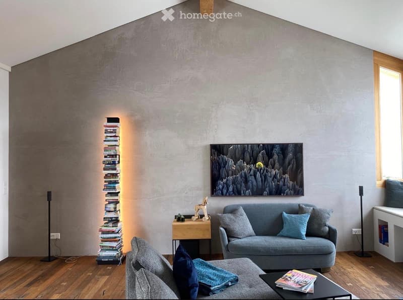 Modern living room with grey sofa, ottoman, coffee table, bookshelf, and artwork on the wall.