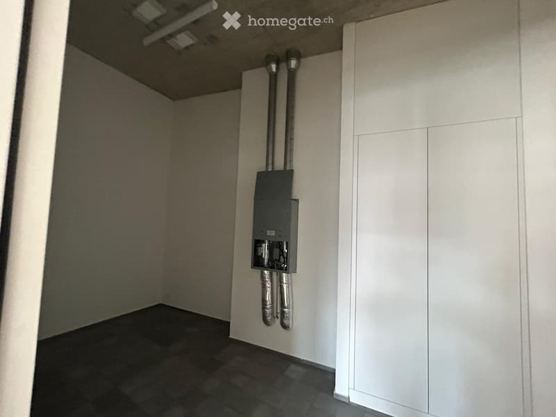 Empty utility room with a black electrical panel, two silver pipes, and a white cabinet.