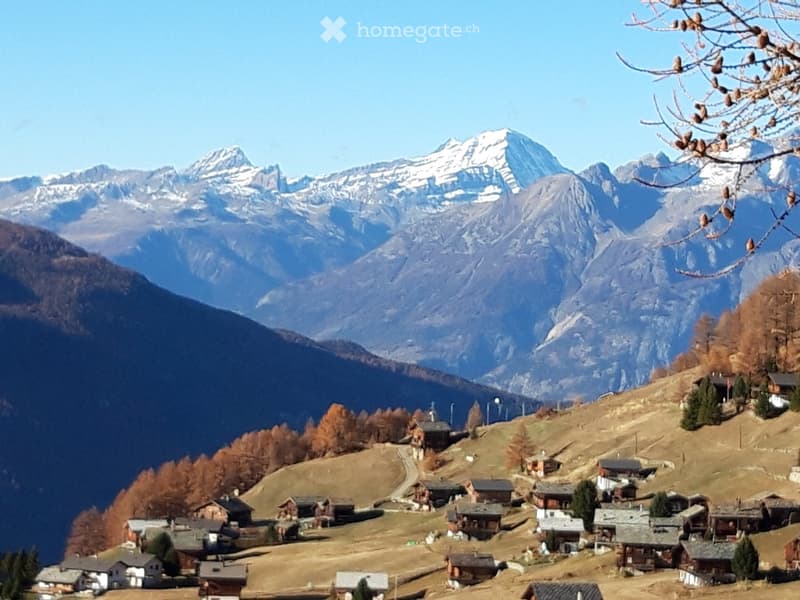 A picturesque mountain village with scattered wooden houses and cabins nestled in a valley, surrounded by snow-capped mountains and autumn-colored trees.
