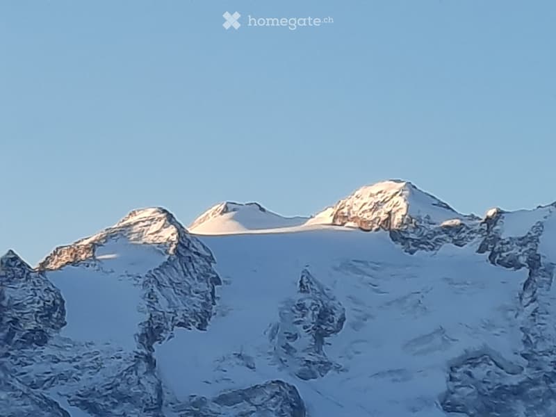 A mountain range with snow-covered peaks and rocky ridges under a clear blue sky.